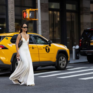a person in a white dress and sunglasses standing in the middle of a street