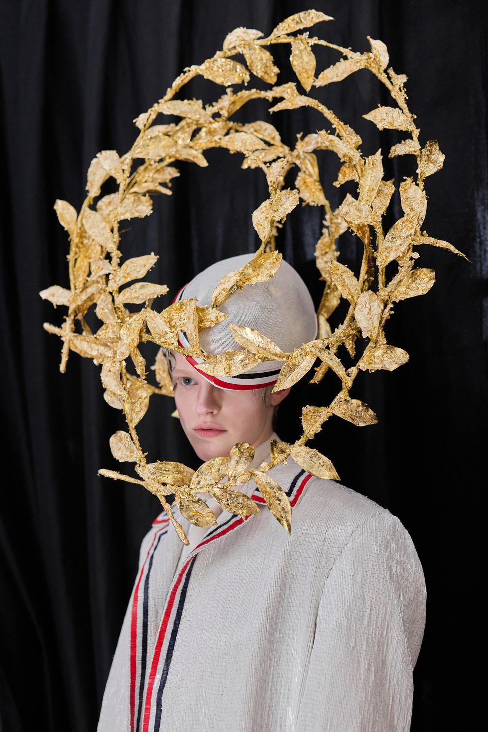 a person in a white blazer and hat with a gold laurel headpiece