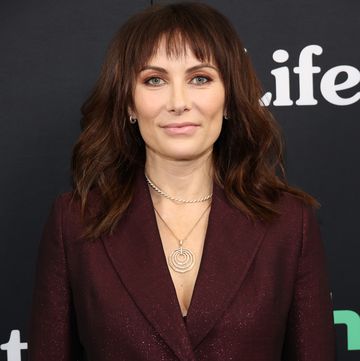 laura benanti, a woman with brown hair worn down in loose waves with a fringe, standing looking straight at the camera with a slight smile, wearing a dark red sparkle suit