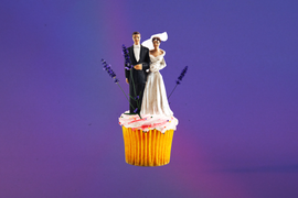 a bride and groom wedding topper on a pink frosted cupcake displayed against a solid purple background