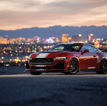 a red sports car on a road with a city in the background