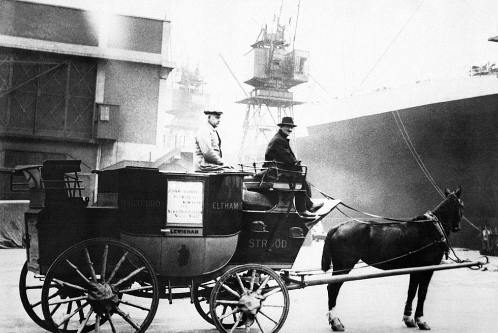 two men sit on a stagecoach carriage attached to a horse