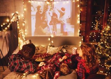 happy family in checkered pajamas mother father and children watching projector, film, movies with popcorn in christmas holiday evening at home 