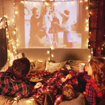 family mother father and children watching projector, film, movi happy family in checkered pajamas mother father and children watching projector, film, movies with popcorn in christmas holiday evening at home