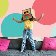 girl standing on a couch, wearing a cardboard box with a mask over her head