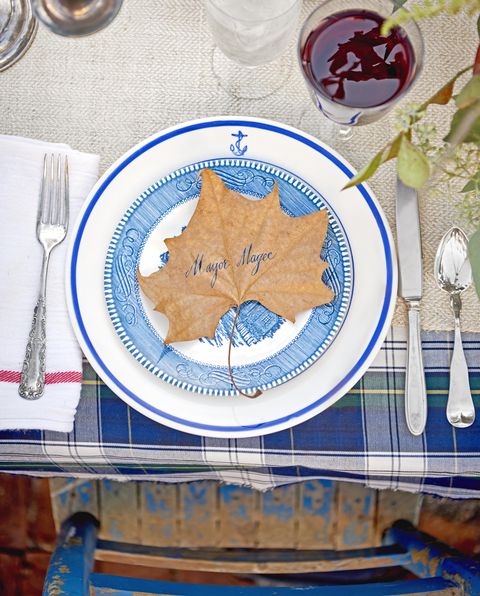 large fall leaf made into place card with name mayor magee penned in blue ink, atop blue and white place setting