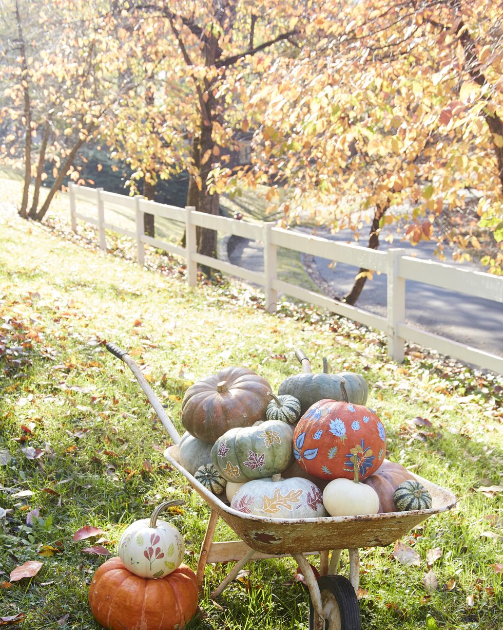 vintage wheelbarrow piled high with pumpkins painted and decorated with fall leaf designs