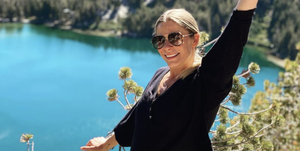 leann rimes posing in front of a lake and mountain landscape with one hand raised