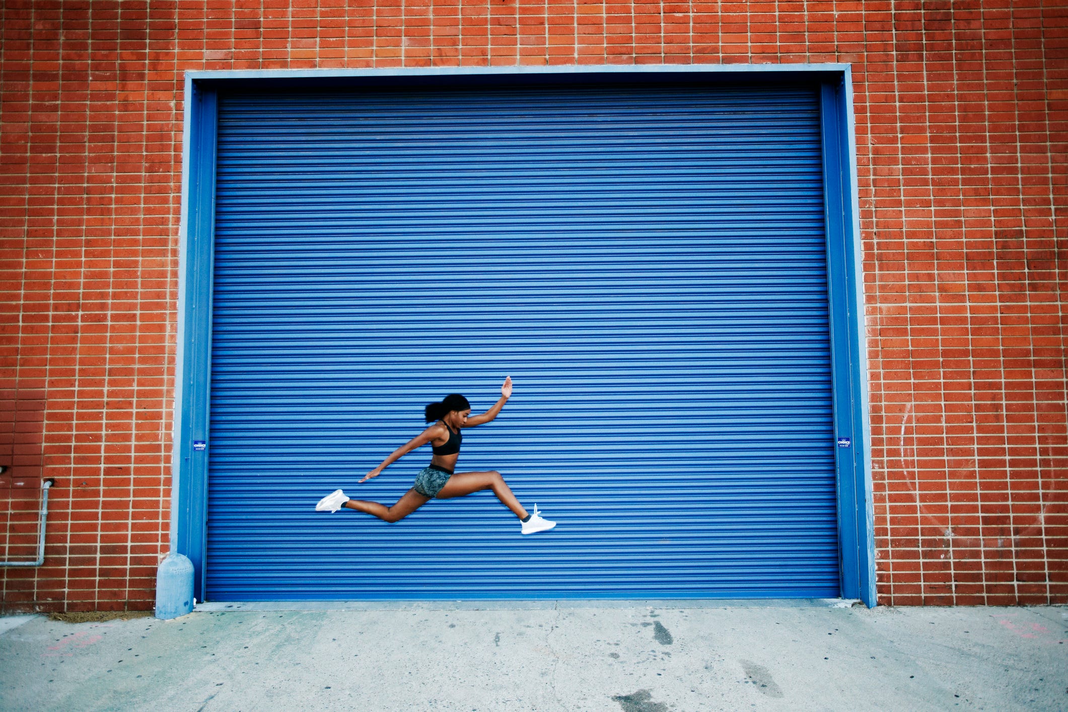 Mixed Race woman running and jumping near blue garage door