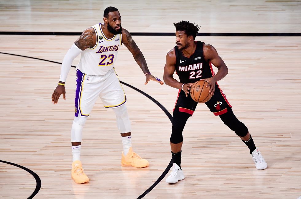 lebron james, wearing a white los angeles lakers jersey, covers jimmy butler, wearing a black miami heat jersey, on a basketball court