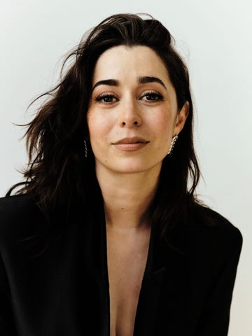 a person with long dark hair wearing a black outfit against a light background