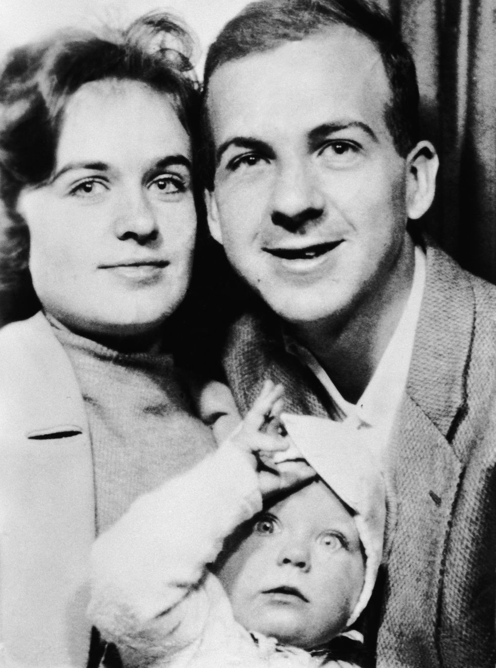 marina oswald and lee harvey oswald embrace for a photo while holding a baby girl