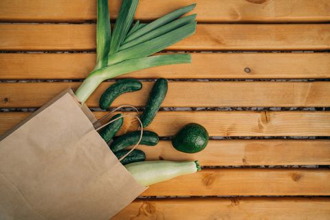 leek, vegetable marrows, zucchini, cucumbers, avocado in craft paper bag on timber planks