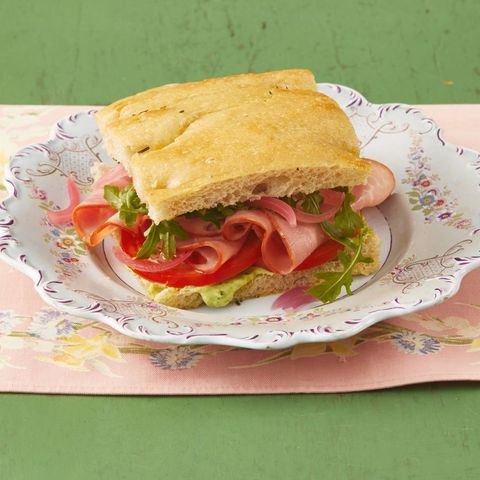 ham sandwich with arugula and pesto mayo on white floral plate and pink linen green background