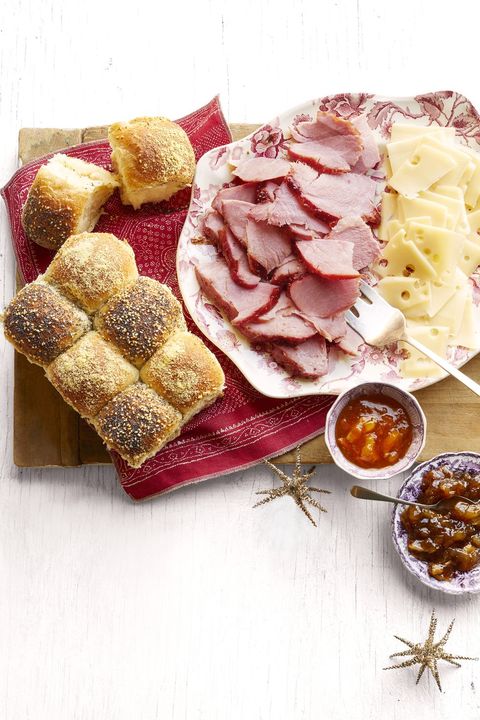 honey glazed ham and checkerboard rolls on platter with cheese slices and bowls of jam