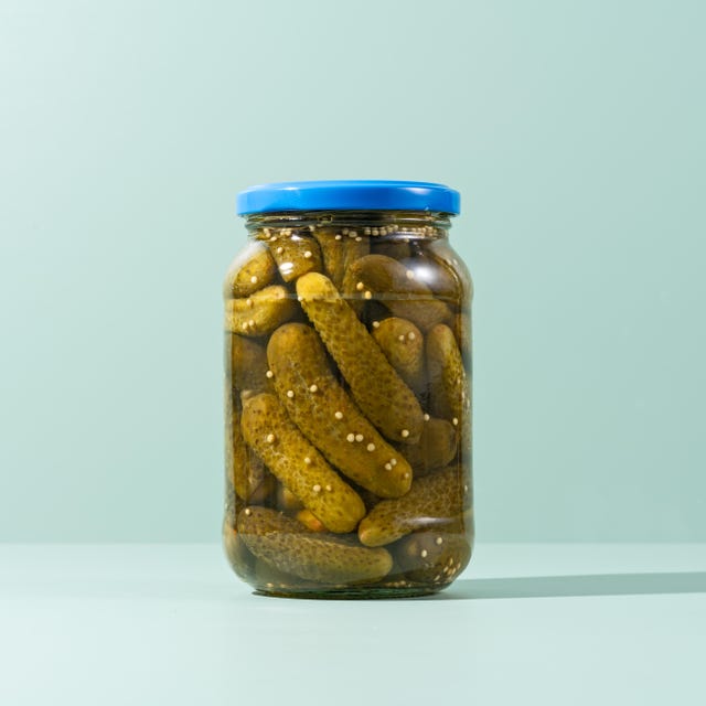 pickles, preserved gherkins in glass jar on green background front view