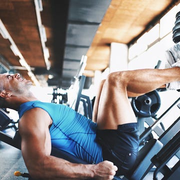 closeup side view of late 20's muscular man doing a leg press exercise at a gym he's wearing blue sleeveless shirt and black trunks