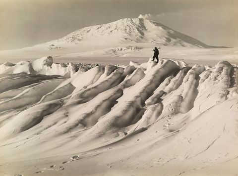 Een lid van de Terra Novaexpeditie uit 1910 staat op een ijsberg voor Mount Erebus de op een na hoogste vulkaan van Antarctica Het laatste team van Robert Falcon Scott wist de Zuidpool te halen maar de vijf mannen kwamen allemaal om op de terugreis