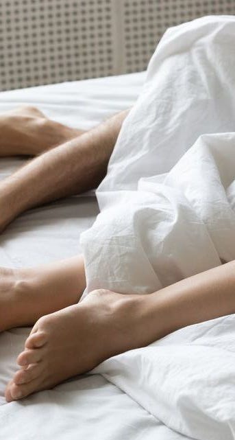 Legs of couple lying under white duvet relaxing in bed