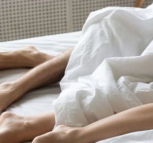 Legs of couple lying under white duvet relaxing in bed