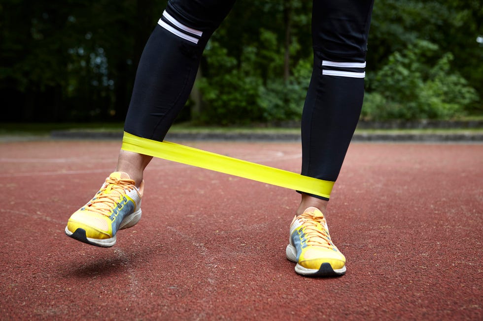 legs of young woman training in park, stretching resistance band