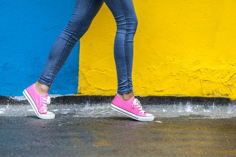 legs of a woman walking in jeans and pink sneakers against yellow and blue wall