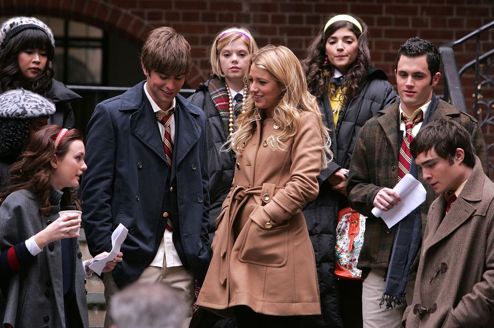 nine teenage actors stand on steps with coats on, looking around and some smiling