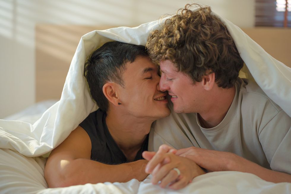 leisurely gay men kissing under bed covers