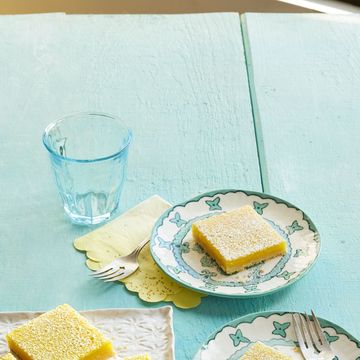 lemon bars on white platter and two plates blue surface