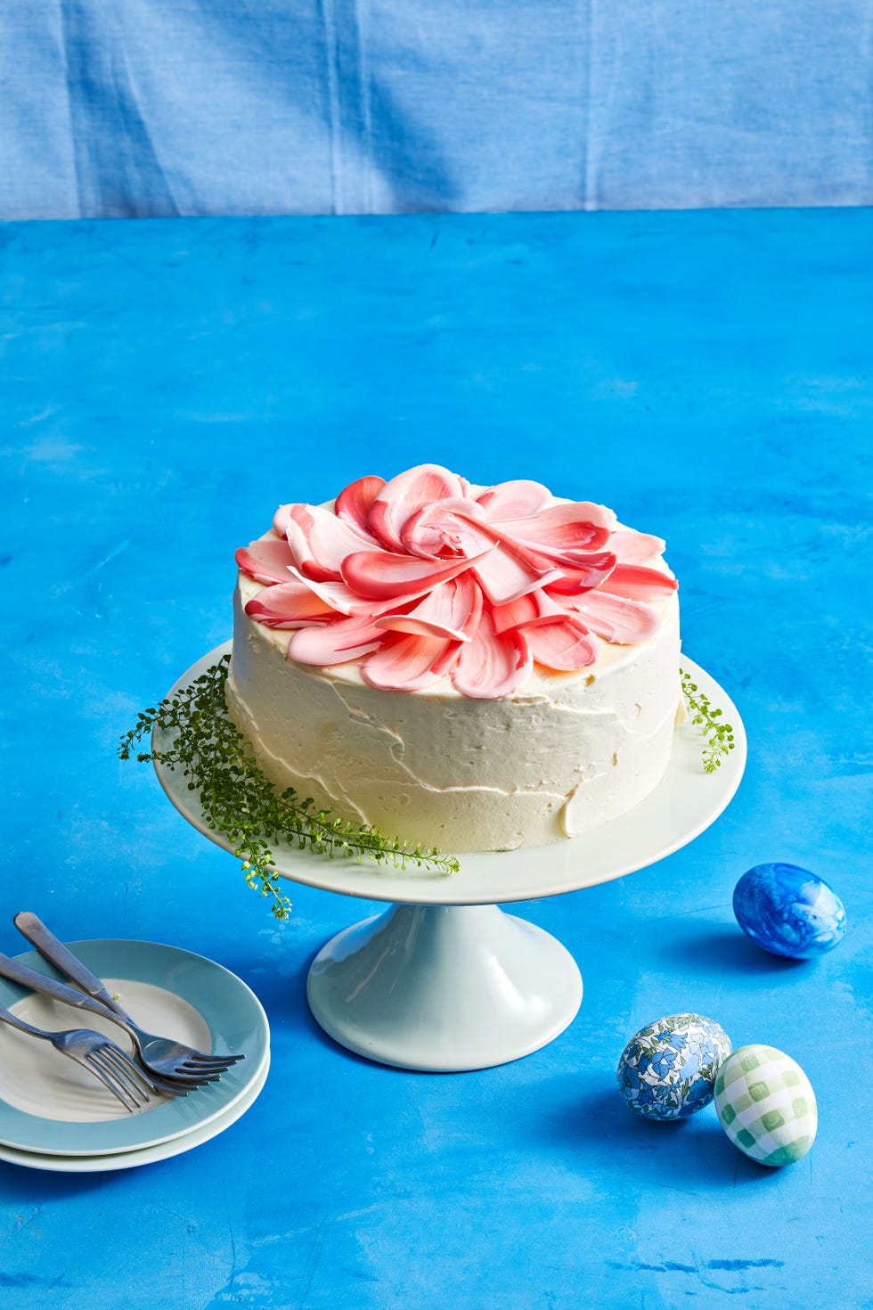 white frosted cake with pink flower petals on top against a blue background