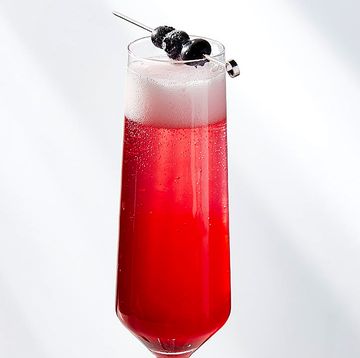 purple pink bubbly drink in a champagne glass garnished with three blueberries