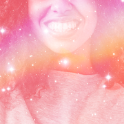 the bottom half of a woman's face is seen behind a rainbow filter, she is smiling widely and has long, curly hair