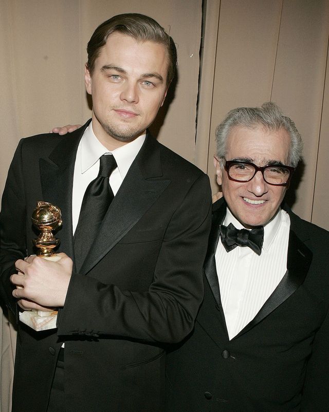 leonardo dicaprio and martin scorsese smile for a photo together while standing, dicaprio holds a golden globe statuette and scorsese has one arm around dicaprios shoulders, both men wear black suits and ties with white collared shirts