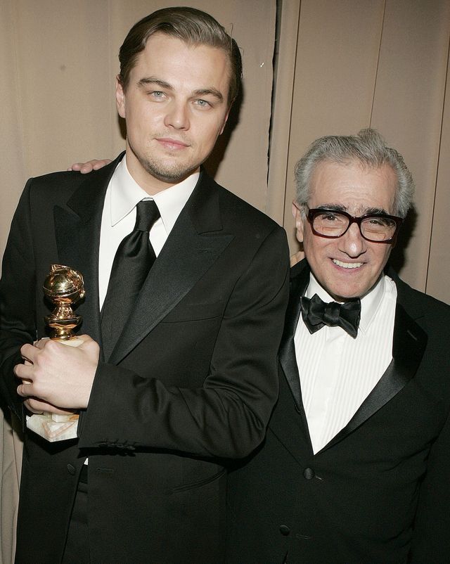 leonardo dicaprio and martin scorsese smile for a photo together while standing, dicaprio holds a golden globe statuette and scorsese has one arm around dicaprios shoulders, both men wear black suits and ties with white collared shirts