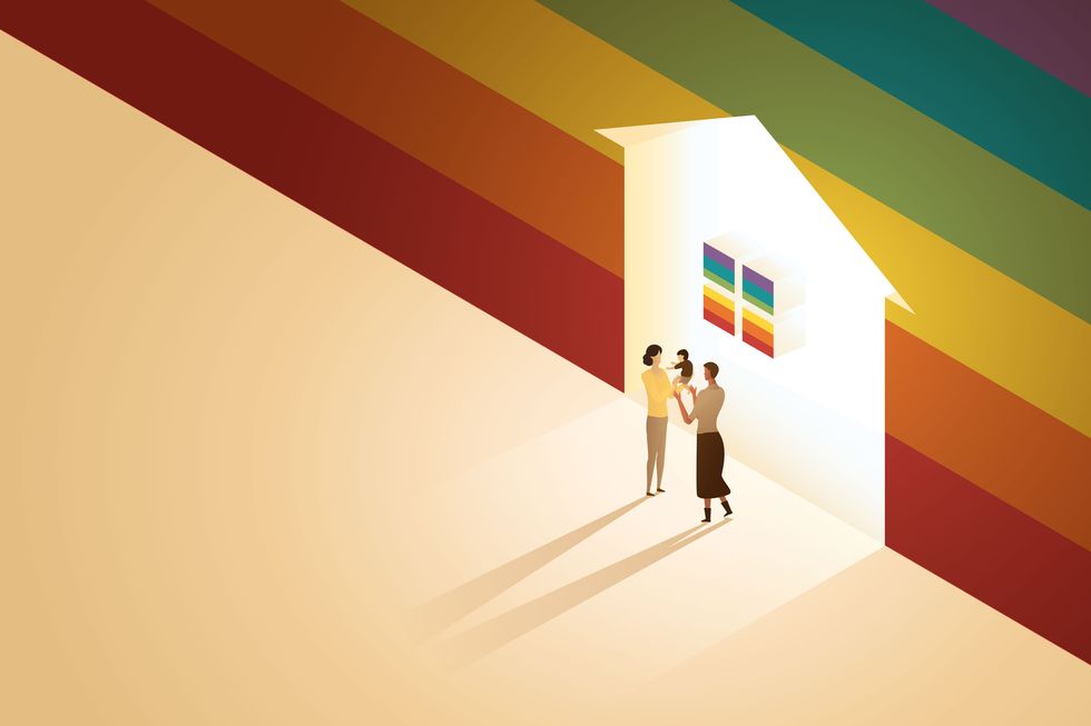 lesbian bisexual couple parents stand in front of a glowing house on wall a rainbow