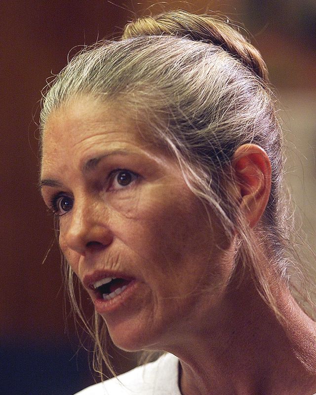 leslie van houten speaks, her hair is styled in a bun on top of her head, and she wears a gray shirt