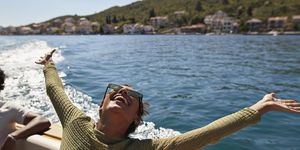 happy young woman with arms raised in motorboat enjoying sunny day