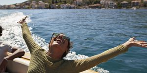 happy young woman with arms raised in motorboat enjoying sunny day