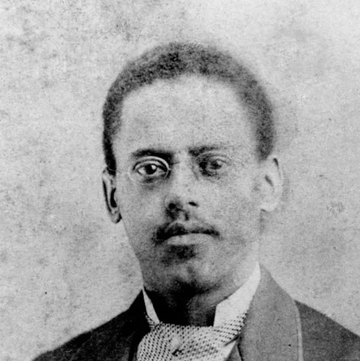 lewis howard latimer stares at the camera in a black and white photo, he wears a suit with a patterned tie and wire framed glasses