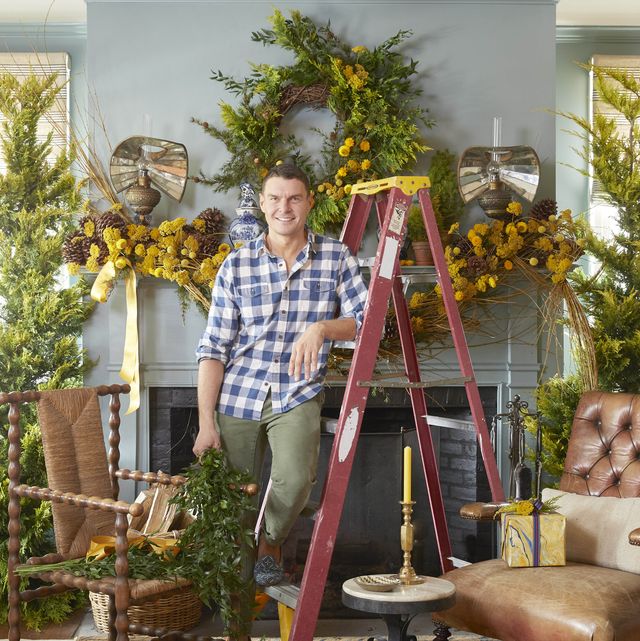 lewis miller stands in front of his mantel leaning against a ladder while he decorates for christmas