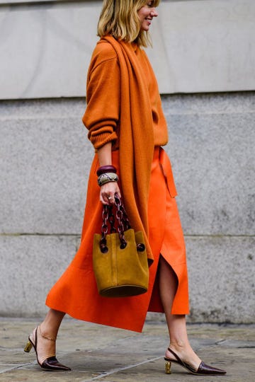 a woman walks in an orange skirt in pointed toe pumps to illustrate a guide to the most comfortable work shoes 2023