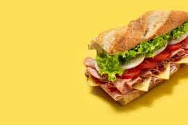 submarine sandwich with ham, cheese, lettuce, tomatoes,onion, mortadella and sausage on yellow background