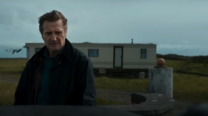 liam neeson in the land of saints and sinners movie, his character stands in front of a caravan and looks concerned