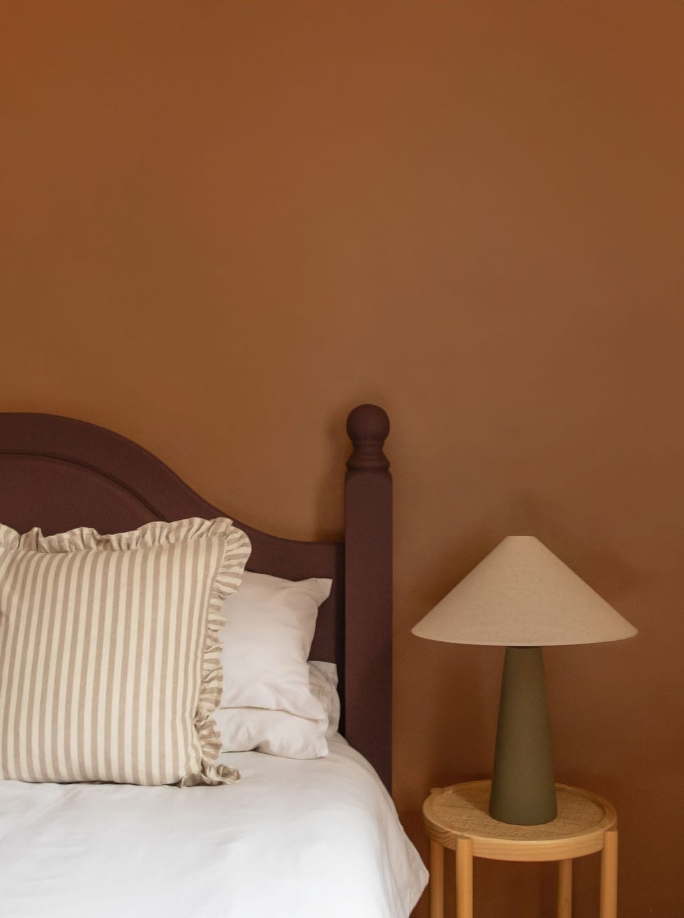 a cosy brown bedroom featuring a bed with a striped pillow and a lamp on a side table