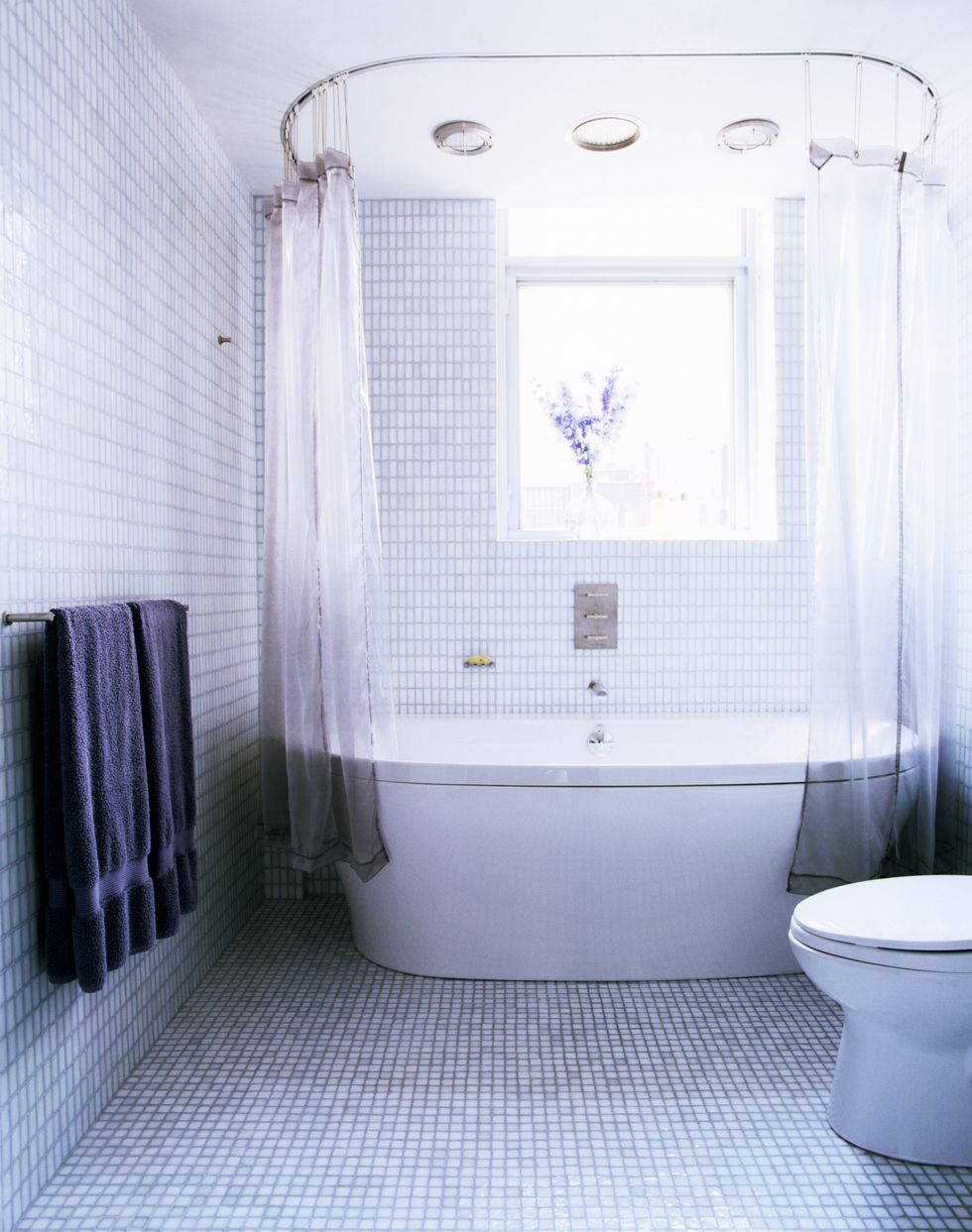 light blue tiled bathroom with white bathtub by window