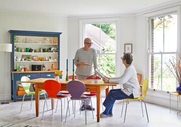 creative dining space featuring a custom oak topped table repurposed from an old desk, repainted dresser, and mismatched colourful chairs against off white walls