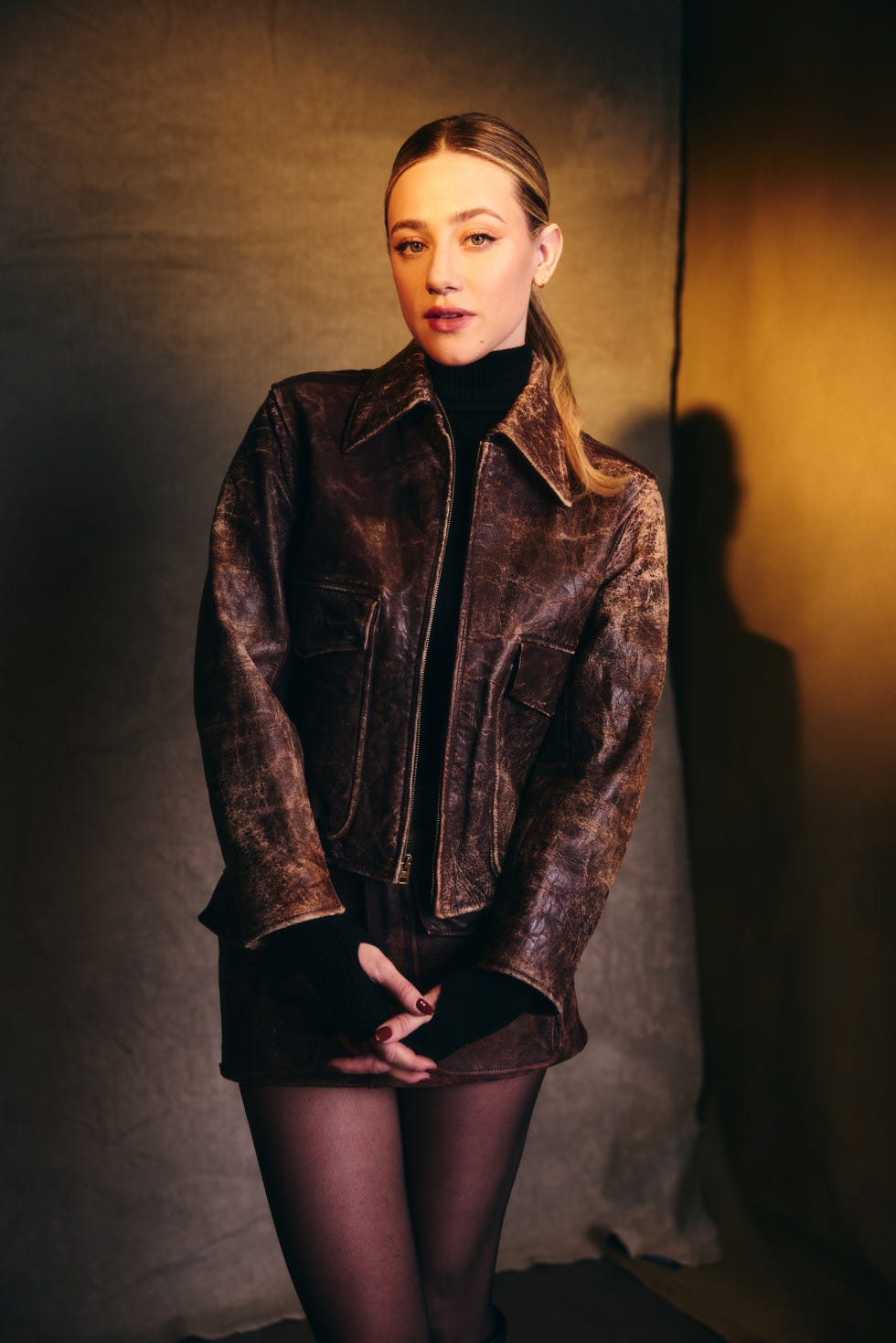 fashion model wearing a brown leather jacket and black outfit in a studio setting