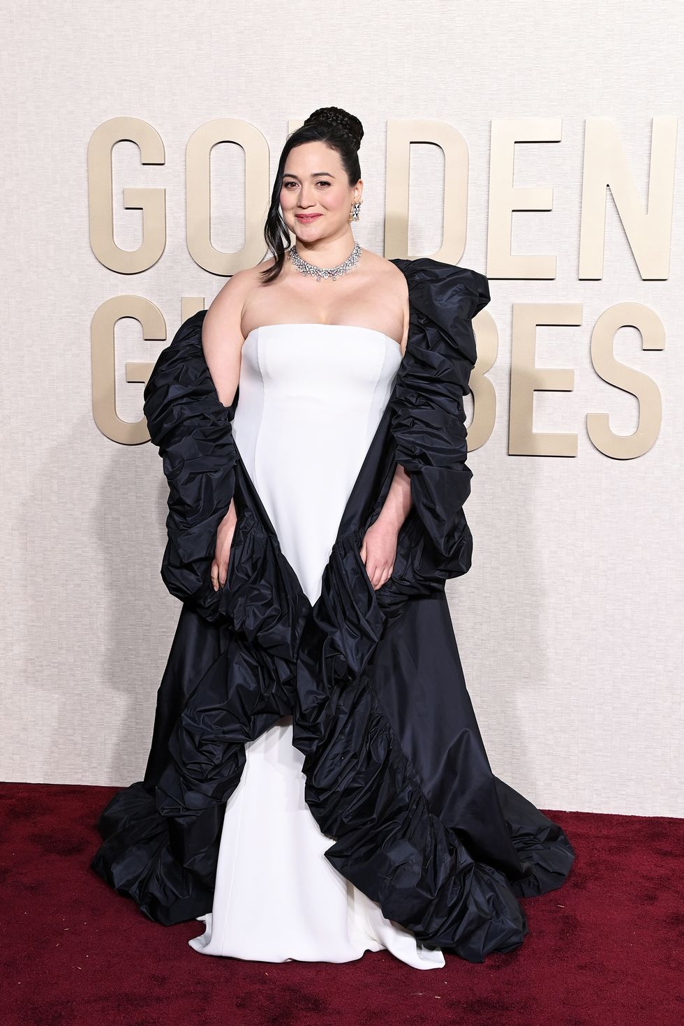 Lily Gladstone con vestido blanco y abrigo negro en los Globos de Oro