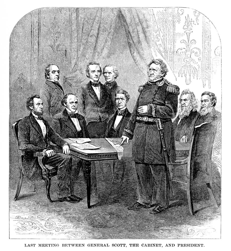 an engraving of abraham lincoln meeting with his cabinet, he sits in a chair in front of a table at far left and wears a suit, four other men are also sitting at the table, and four men are standing around the table, including a general in a military uniform