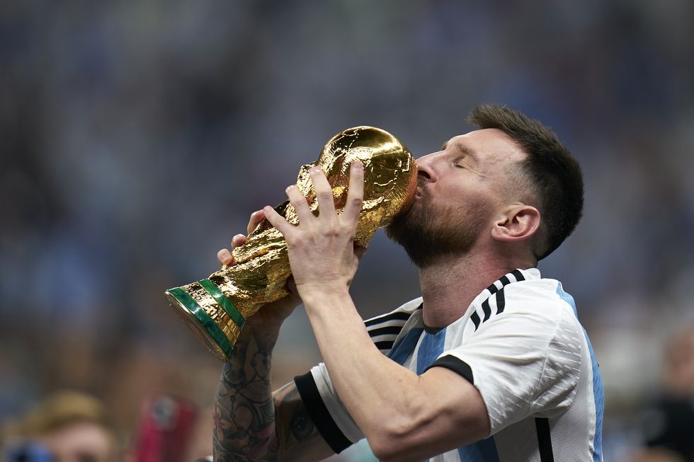lionel messi kisses a gold trophy after his team won the 2022 fifa world cup, he wears an argentina national team jersey and holds the trophy in his hands